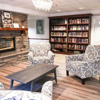 A cozy reading room featuring armchairs, a fireplace, and a bookshelf filled with books.
