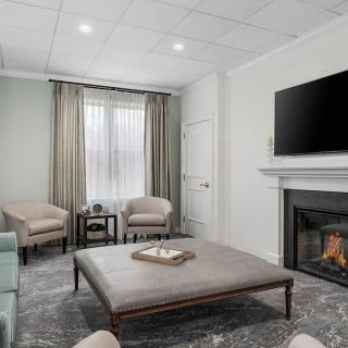 A modern living room featuring a large ottoman, cozy chairs, a fireplace, and a wall-mounted television.