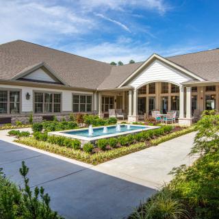 A beautiful house with a landscaped garden and a small central pool under a clear blue sky.