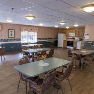 A spacious dining room with several tables and chairs, adjacent to a kitchen area.
