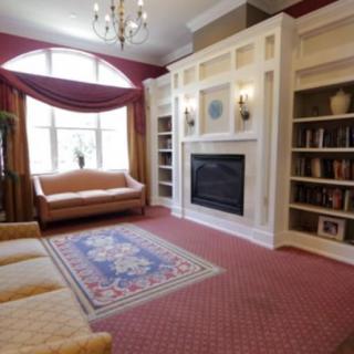 A cozy living room with a fireplace surrounded by built-in bookshelves, featuring a large window and comfortable sofas on a patterned carpet.