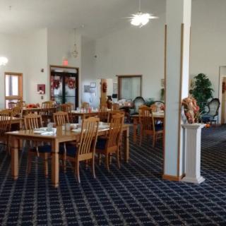 An indoor dining area with wooden tables and chairs arranged on a carpeted floor.