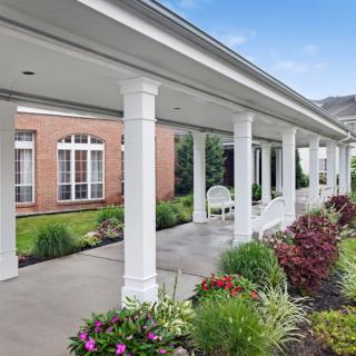 A covered walkway with white columns and landscaped garden.