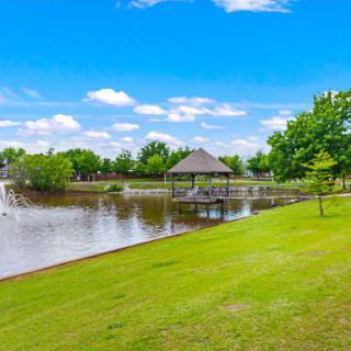 A peaceful park scene with a gazebo by the lake under a bright blue sky.