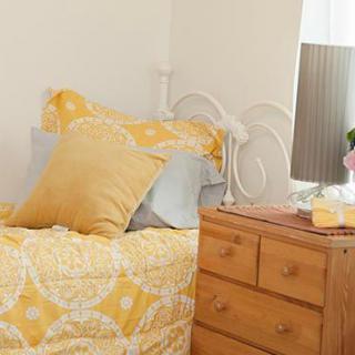 A cozy bedroom corner featuring a bed with yellow bedding, a wooden dresser, and a decorative lamp.