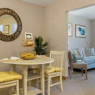 A cozy dining area with a round table and chairs, featuring a decorative mirror and an adjacent living room.
