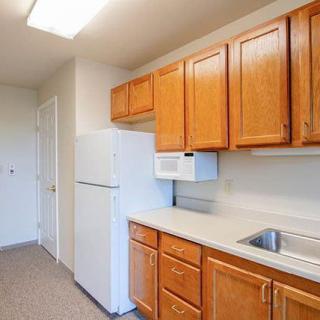 A simple kitchen with wooden cabinets, a refrigerator, microwave, and sink.