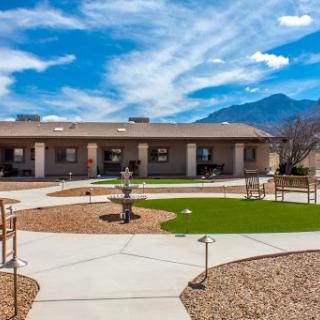 A serene outdoor area featuring a building, pathways, and landscaped gardens under a clear blue sky.