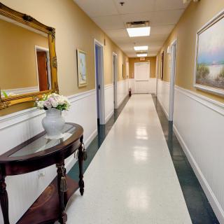 A well-lit hallway with a decorative table and mirror, adorned with paintings on the walls.