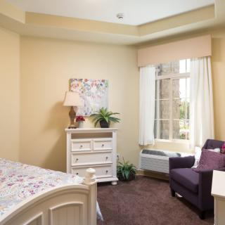 A cozy bedroom with soft lighting, featuring a comfortable chair by the window and tasteful decor.