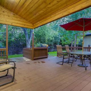 A cozy outdoor deck area featuring comfortable seating and a dining table under a red umbrella, surrounded by lush greenery.