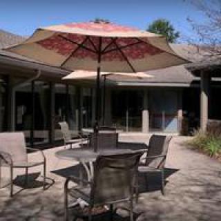A sunny courtyard with outdoor furniture, including a table and chairs under a patio umbrella.