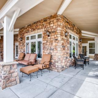 A spacious outdoor patio with stone walls, featuring comfortable seating and a table under a covered area.
