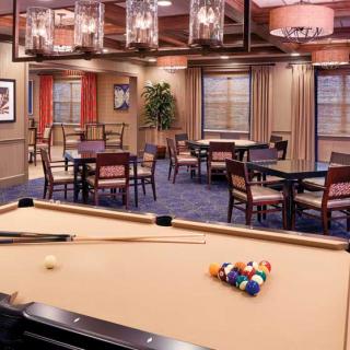 A cozy game room featuring a pool table and seating area, illuminated by stylish overhead lighting.