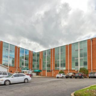 A commercial building with large glass windows and a parking lot on a cloudy day.