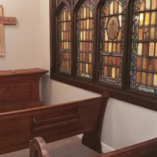 A serene chapel interior featuring wooden pews, a cross, and intricate stained glass windows.