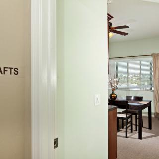 A view of a crafts room with a dining table and ceiling fan, seen through an open doorway.