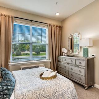 A cozy bedroom with a large window, dressed in neutral tones and elegant furnishings.
