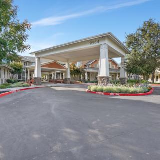 A large building entrance with a covered driveway and landscaped surroundings.