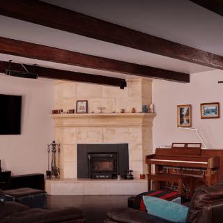 A cozy living room featuring a stone fireplace, wooden piano, and exposed wood beams.