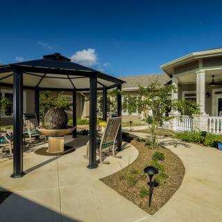 A well-maintained garden featuring a gazebo and a modern building under a clear blue sky.