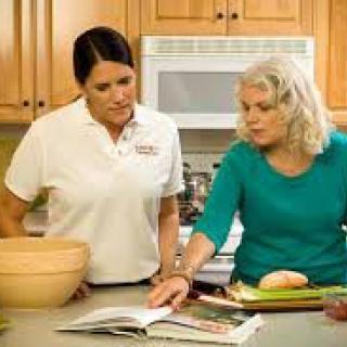 Two women in a kitchen preparing food, consulting a recipe book.