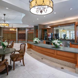 A well-furnished lobby with a reception desk and seating area, decorated with chandeliers and floral arrangements.