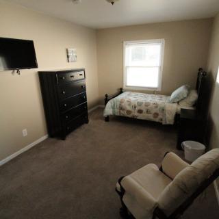A tidy bedroom with a bed, dresser, mounted TV, and a window.