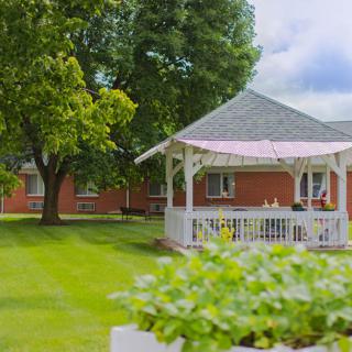 A charming gazebo in a lush, green garden setting with nearby buildings.