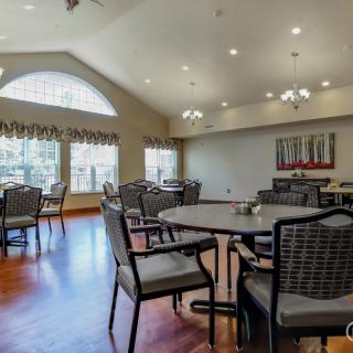 A spacious dining room with tables and chairs, featuring large windows and bright lighting.