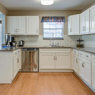 A modern kitchen with white cabinets, a stainless steel dishwasher, and wooden flooring.