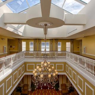 An elegant lobby featuring a stunning chandelier and skylight, complemented by yellow walls and a beautiful balcony.