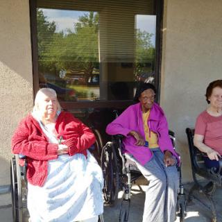 Three elderly women enjoying a sunny day outdoors in their wheelchairs.