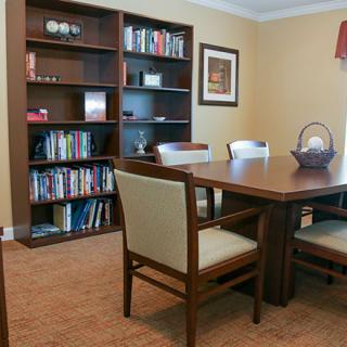 A cozy meeting room with a wooden table, chairs, and a filled bookshelf.