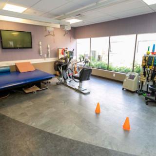 A rehabilitation room equipped with exercise equipment, including a bicycle machine and treatment table, with cones on the floor.