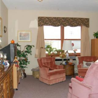 A cozy living room with armchairs and a television, decorated with plants and curtains.