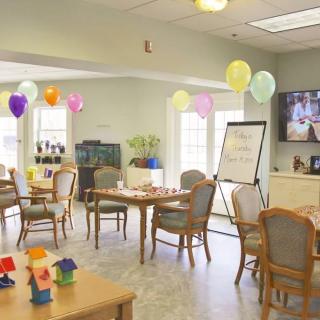 A decorated community center room with tables, chairs, and colorful balloons.