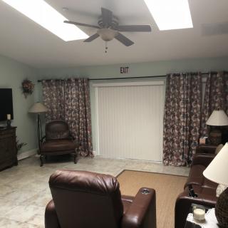 A cozy living room with leather armchairs, a ceiling fan, and patterned curtains.