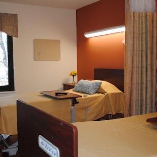 A well-furnished hospital room with a bed, window, and soft lighting.