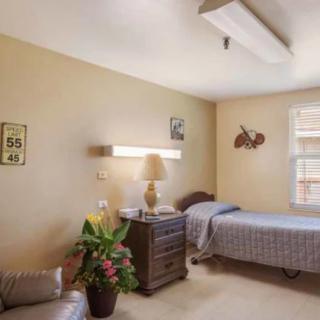 A cozy bedroom with a single bed, lamp, and dresser.