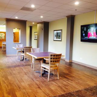 A modern lounge area with wooden flooring, tables and chairs, adorned by a wall-mounted television.
