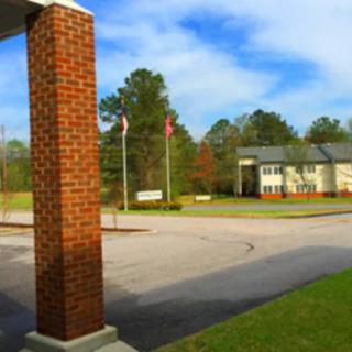 A view of a brick-columned structure overlooking a quiet parking lot, with flags and trees in the background under a cloudy sky.
