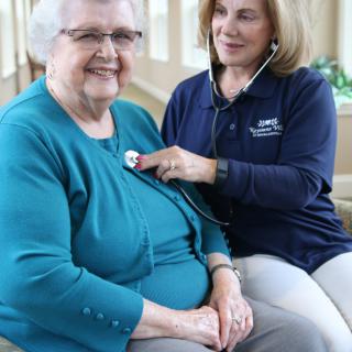 A healthcare professional uses a stethoscope to examine an elderly woman.