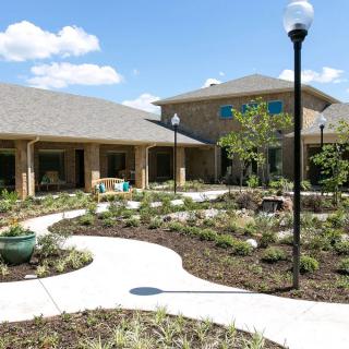 A modern building surrounded by landscaped gardens and pathways under a clear blue sky.