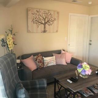 A cozy living room with a gray sofa, colorful cushions, and a tree wall art piece.