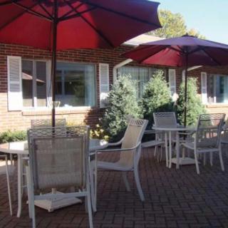 A sunny patio with tables, chairs, and red umbrellas.