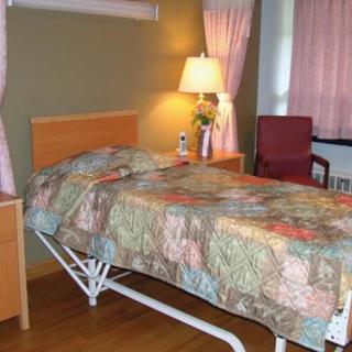 A hospital room with a single bed, floral bedspread, lamp, and pink curtains.