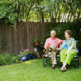 An elderly couple sitting together on a bench in a garden.