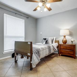 A small bedroom with a hospital bed, nightstand, and lamp under a ceiling fan.
