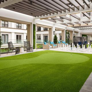 A modern outdoor patio with artificial turf and comfortable seating under a pergola.